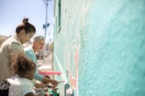 Mujeres voluntarias pintando mural en pared soleada - foto de stock