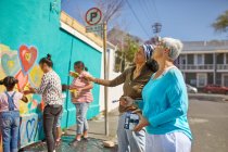 Volontari comunitari che dipingono vivaci murales su soleggiate mura urbane — Foto stock