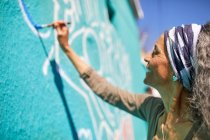 Senior woman painting mural on sunny wall — Stock Photo
