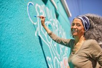 Retrato feliz sênior feminino voluntário pintura na parede ensolarada — Fotografia de Stock