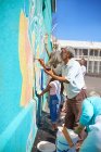 Общественные волонтеры рисуют яркие фрески на солнечной городской стене — стоковое фото