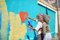 Feliz pareja de ancianos pintando mural en forma de corazón en la pared soleada - foto de stock