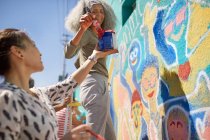 Женщины-волонтеры рисуют яркие общественные фрески на солнечной городской стене — стоковое фото