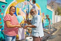 Portrait happy community volunteers painting mural on sunny urban wall — Stock Photo