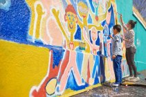 Mãe e filho voluntários pintando mural vibrante na parede ensolarada — Fotografia de Stock