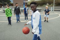 Portrait confident african american boy playing basketball in schoolyard — Stock Photo