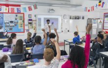 Insegnante di sesso maschile lezione di guida a schermo di proiezione in classe con gli studenti alzando le mani — Foto stock