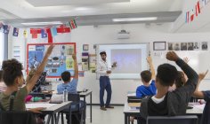 Молодші Учні середньої школи, що піднімають руки для вчителя провідний урок в класі — стокове фото