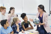 Attenti studenti delle scuole medie guardando insegnante di geografia con globo — Foto stock