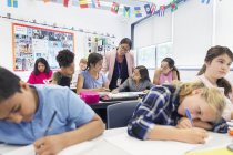 Жінка-вчителька допомагає молодшим школярам робити домашнє завдання за столом у класі — стокове фото
