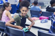 Retrato sorridente, confiante estudante do ensino médio júnior com fones de ouvido na mesa em sala de aula — Fotografia de Stock