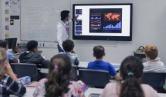 Professor do sexo masculino lição de liderança na tela sensível ao toque de televisão em sala de aula — Fotografia de Stock