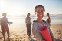 Retrato mulher feliz com tapete de ioga na praia ensolarada durante retiro de ioga — Fotografia de Stock