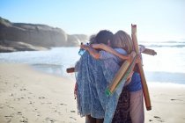 Women friends with yoga mats hugging on sunny beach during yoga retreat — Stock Photo