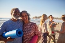 Portrait happy senior couple with yoga mats on sunny beach during yoga retreat — Stock Photo