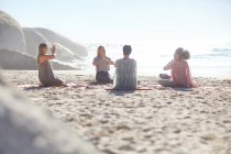 Group meditating in circle on sunny beach during yoga retreat — Stock Photo