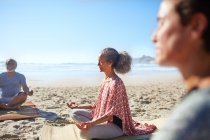 Спокойная пожилая женщина медитирует на солнечном пляже во время йоги — стоковое фото