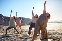 Groupe pratiquant le yoga posture guerrière inverse sur la plage ensoleillée pendant la retraite de yoga — Photo de stock