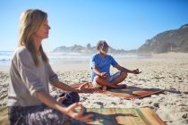 Persone serene che meditano sulla spiaggia soleggiata durante il ritiro yoga — Foto stock