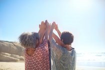 Mulheres com braços levantados em círculo na praia ensolarada durante retiro de ioga — Fotografia de Stock