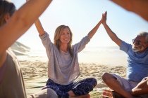 Amigos felices uniendo sus manos en círculo en la soleada playa durante el retiro de yoga - foto de stock