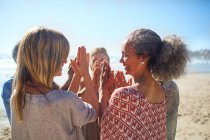 Mulheres amigas com as mãos fechadas em círculo na praia ensolarada durante retiro de ioga — Fotografia de Stock