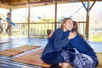 Happy mother and daughter hugging on yoga mats in hut during yoga retreat — Stock Photo