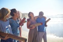 Happy friends with yoga mats bonding on sunny beach during yoga retreat — Stock Photo