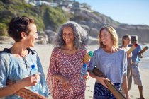 Women friends with yoga mats talking on sunny beach during yoga retreat — Stock Photo