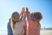 Women friends raising hands in circle during yoga retreat on sunny beach — Stock Photo