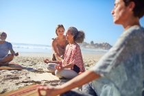Serene women meditating on sunny beach during yoga retreat — Stock Photo