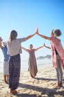 Група, що з'єднує руки в колі на сонячному пляжі під час відступу йоги — стокове фото