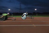 Atletas parapléjicos corriendo por pista deportiva en carrera en silla de ruedas - foto de stock