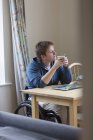 Задумчивая молодая женщина в инвалидной коляске пьет чай за обеденным столом — стоковое фото