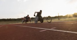 Atletas paraplégicos acelerando ao longo da pista de esportes durante a corrida em cadeira de rodas — Fotografia de Stock