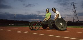 Retrato seguro, atletas parapléjicos en pista deportiva, entrenamiento para la carrera en silla de ruedas por la noche - foto de stock