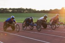 Atletas parapléjicos corriendo por pista deportiva en carrera en silla de ruedas - foto de stock