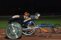 Паралельні спортсмени прискорюються вздовж спортивної траси під час гонки на інвалідних візках вночі — стокове фото