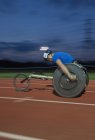 Визначений молодий чоловічий паралельний спортсмен, що перевищує швидкість вздовж спортивної траси в гонці на інвалідних візках вночі — стокове фото