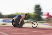 Jeune athlète paraplégique masculin déterminé à accélérer le long de la piste de sport dans une course en fauteuil roulant — Photo de stock