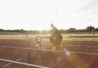 Jeune athlète masculin paraplégique s'entraînant pour la course en fauteuil roulant sur piste de sport ensoleillée — Photo de stock