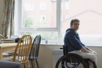Portrait confiant jeune femme assise en fauteuil roulant à la fenêtre — Photo de stock