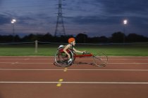 Adolescente chica parapléjico atleta en silla de ruedas carrera en pista deportiva por la noche - foto de stock