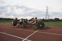 Atletas parapléjicos acurrucados en pista deportiva, entrenamiento para la carrera en silla de ruedas - foto de stock