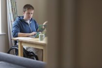 Молода жінка в інвалідному візку використовує ноутбук за обіднім столом — стокове фото