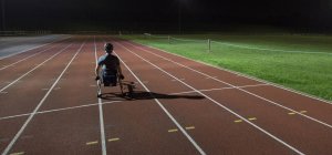 Treinamento de atleta paraplégico para corrida em cadeira de rodas em pista de esportes à noite — Fotografia de Stock