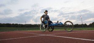 Decidida joven atleta parapléjica entrenando para la carrera en silla de ruedas en pista deportiva - foto de stock