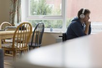 Безтурботний молоду жінку в інвалідному візку, слухати музику з навушниками в вікно — стокове фото