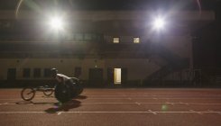 Male paraplegic athlete training for wheelchair race on sports track at night — Stock Photo