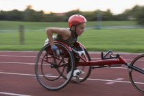 Determined teenage girl paraplegic athlete speeding along sports track in wheelchair race — Stock Photo